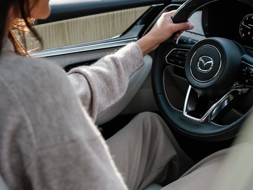 Driver in wool sweater with hands on the wheel inside the CX-90.  
