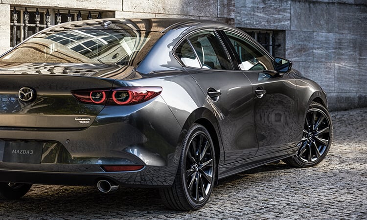 Mazda3 sedan turns its wheels to exit a cobblestone alley way in daylight.