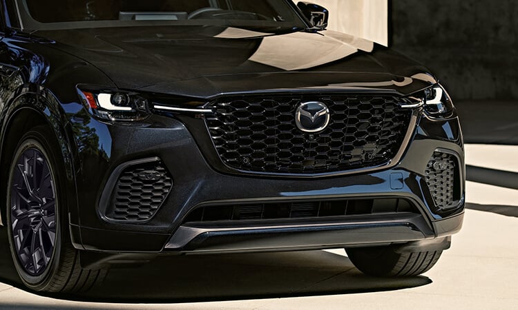 The front hood, grille and Mazda emblem of a Jet Black CX-70 reflect the daylight.