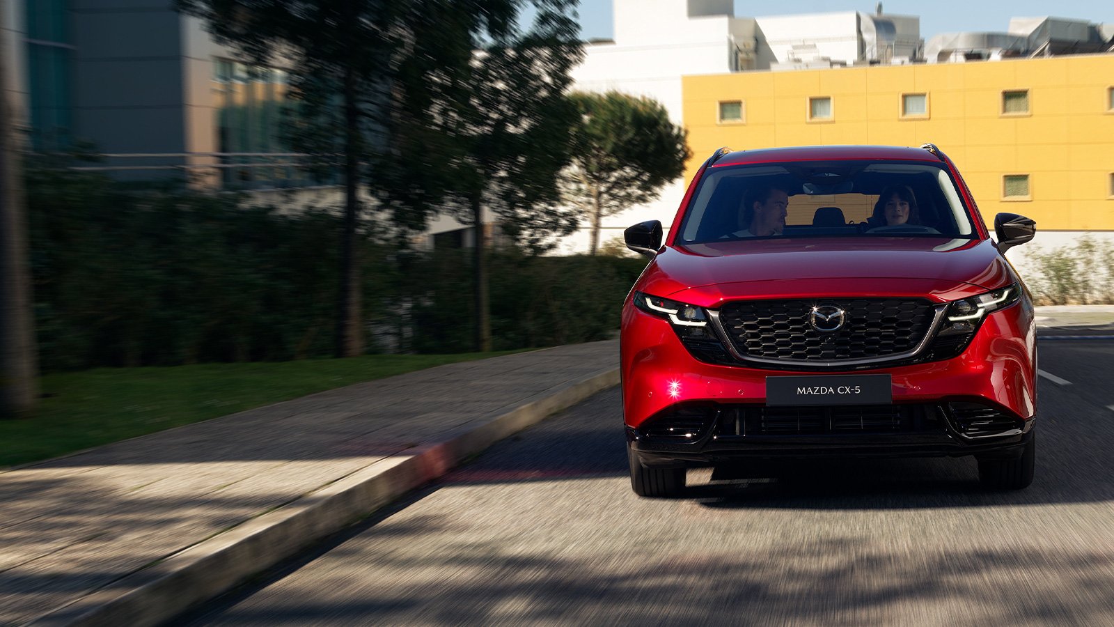 Vue avant d'un Mazda CX-5 rouge vibrant cristal se dirigeant vers la caméra sur une route urbaine.