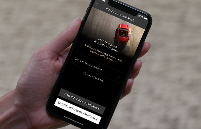 A driver holds a mobile phone with MyMazda app on the screen