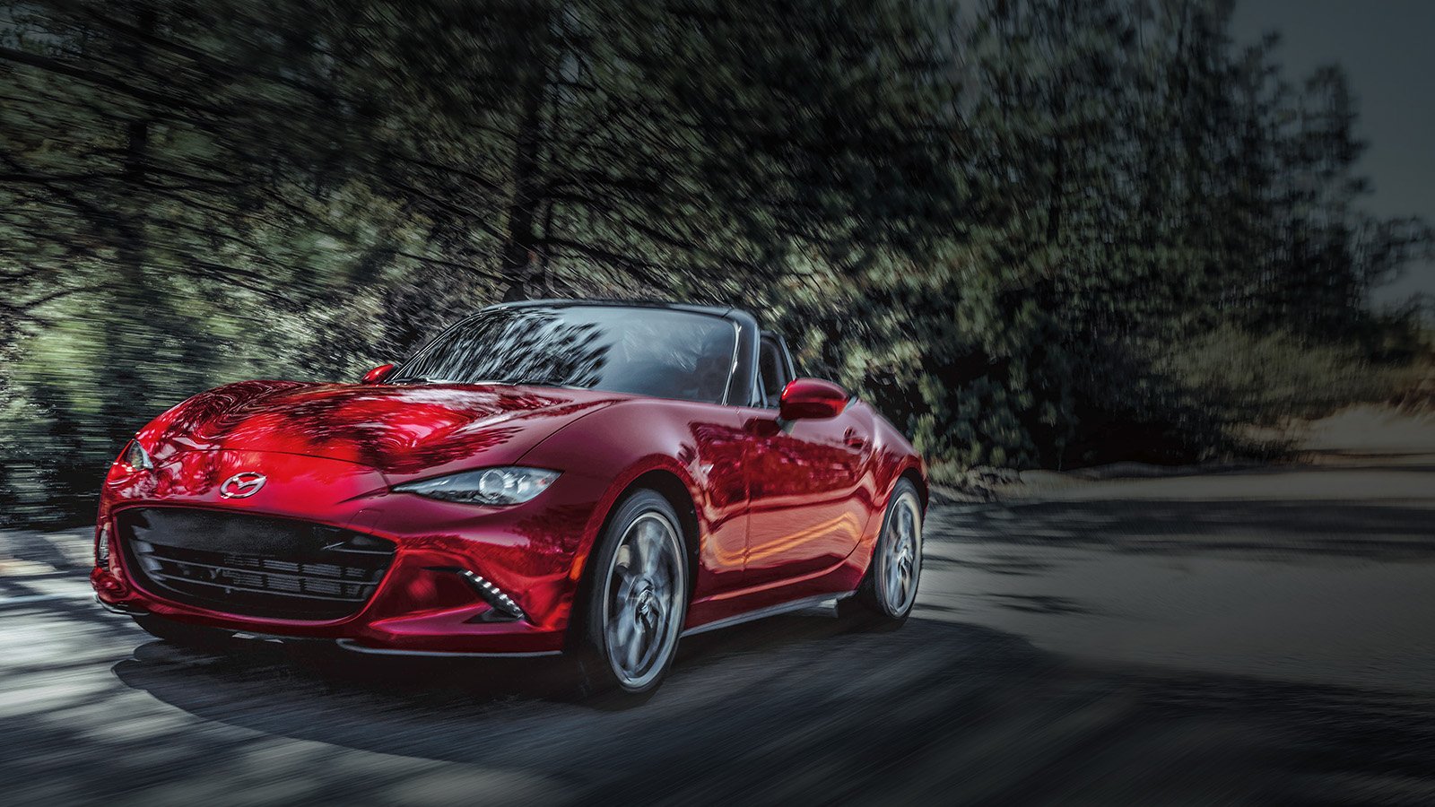 A red Mazda MX-5 Soft Top driving down a forest road.