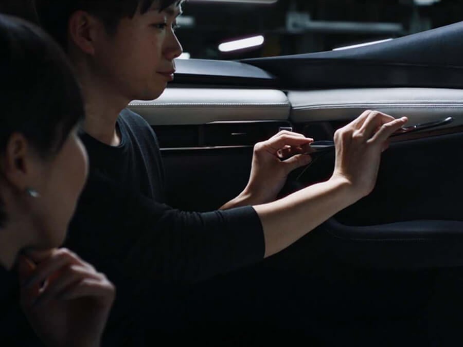 Hands of a Mazda technician catch the light as he makes an adjustment to a car’s interior while a female colleague looks on.