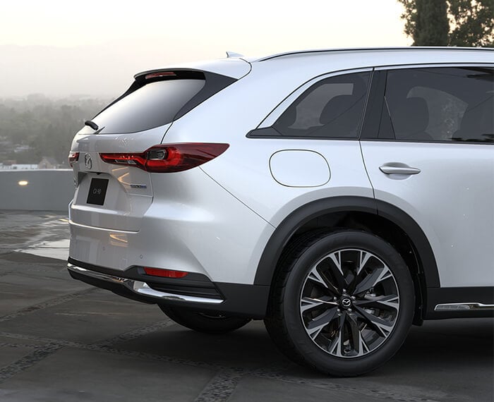 Artisan Red CX-90 almost straight grille on, making a turn in a city block.