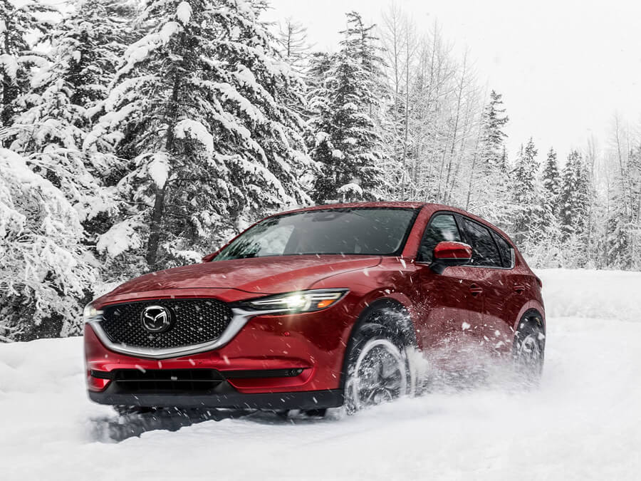 Red Mazda driving on a country road in winter with snow covered trees in background