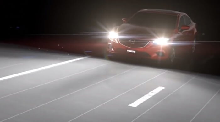 Red Mazda on dark road with high beams switched on