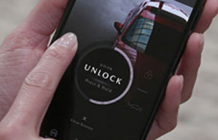 A driver holds a mobile phone with MyMazda app on the screen