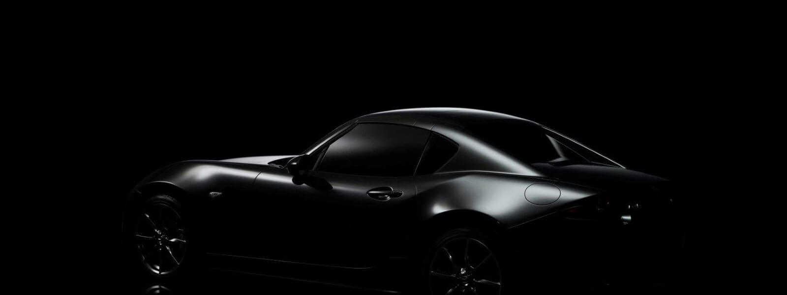 Black Mazda MX-5 RF 2-seat hard-top convertible against a black background.