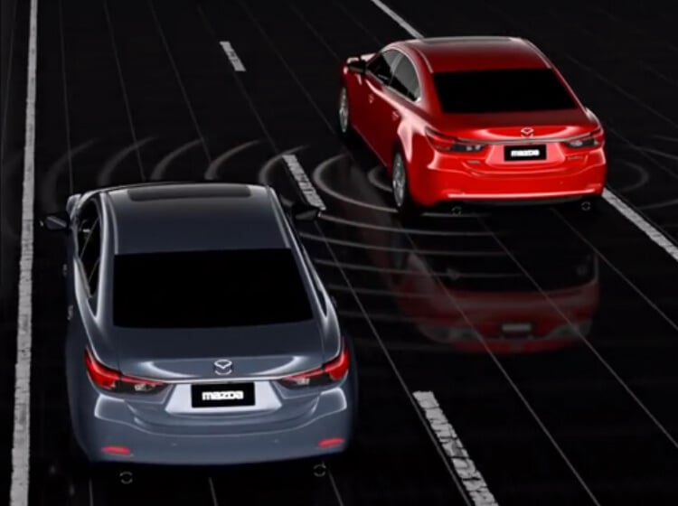 Photo illustration of two Mazdas in separate lanes on a dark highway, with white circular lines emanating from under the lead vehicle to represent Blind Spot Monitoring radar.