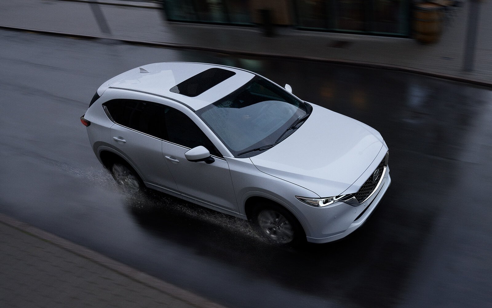 White Mazda CX-5 with closed sunroof driving down urban street in the rain