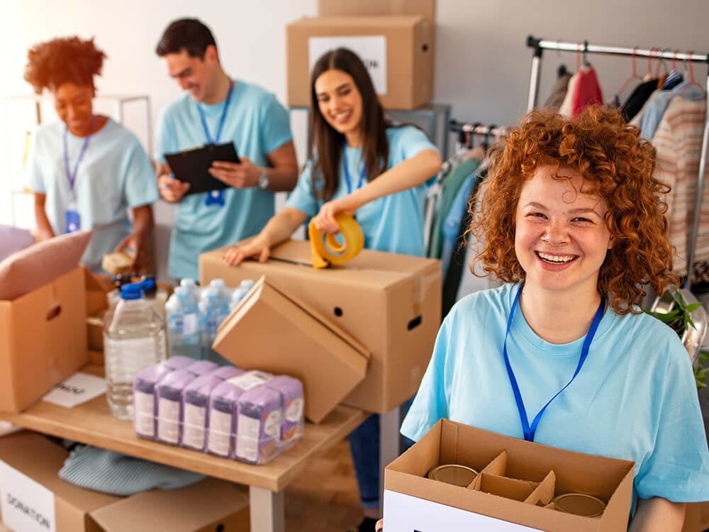 A team of teens in blue tees package up donated goods in boxes for delivery. 