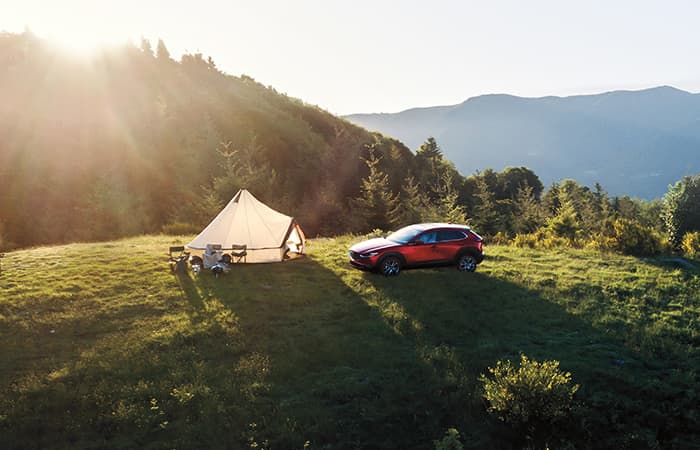 Un véhicule Mazda rouge garé à côté d’une tente dans une zone boisée.