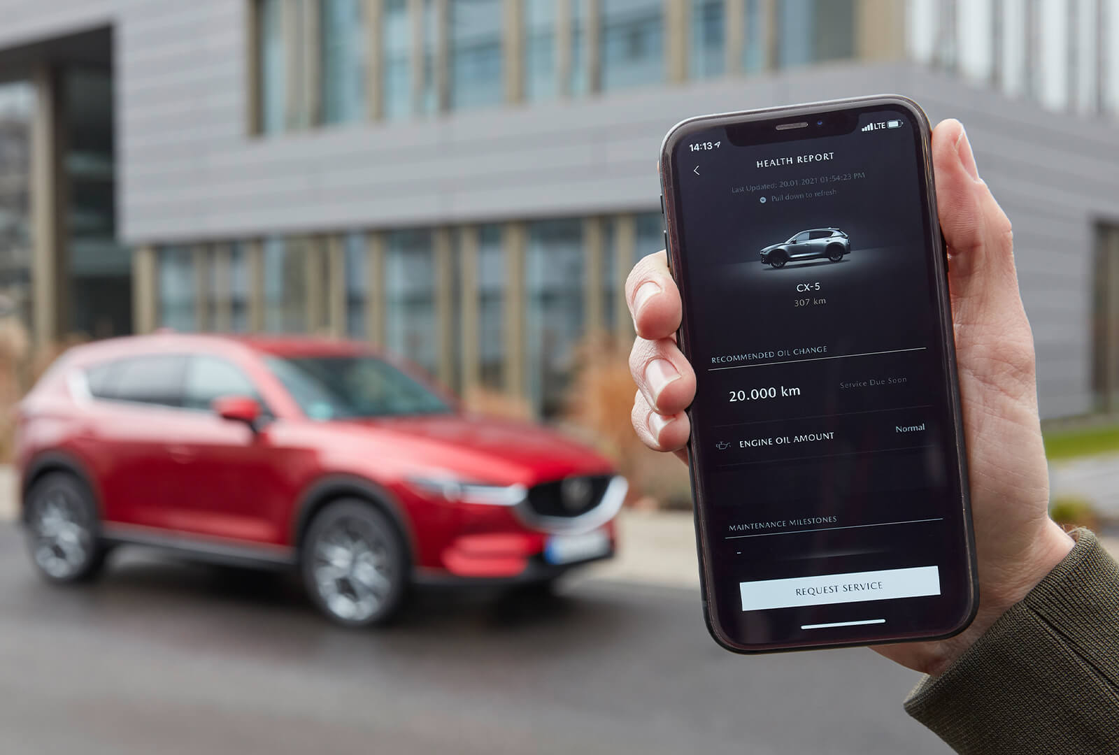 Hand holding up smartphone with MyMazda App displaying CX-5 info.