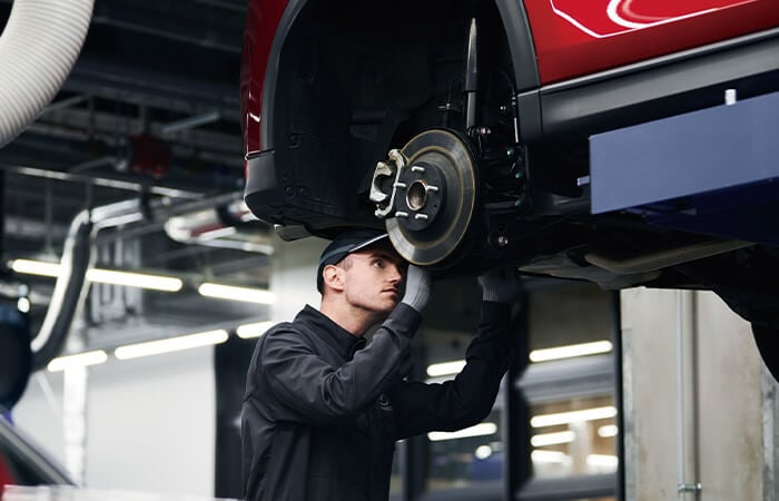 Mazda technician inspects front axle of Mazda on hydraulic lift in service bay.