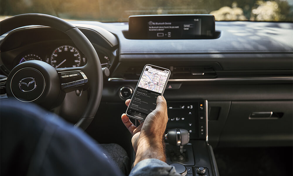 Conducteur tenant un téléphone qui affiche de l’information cartographique, avec l’écran Mazda Connect visible sur le tableau de bord