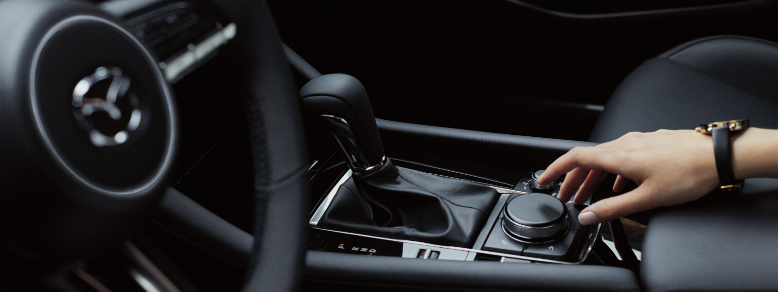 Intérieur d’une Mazda montrant la main droite d’une femme actionnant une commande de la console 