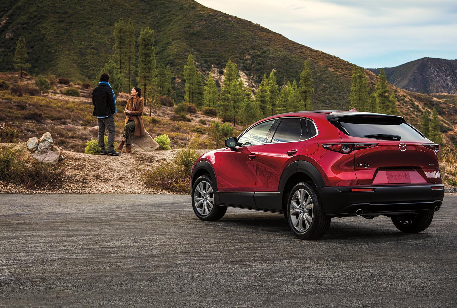 Red Mazda CX-30 parked facing partly forested hillside