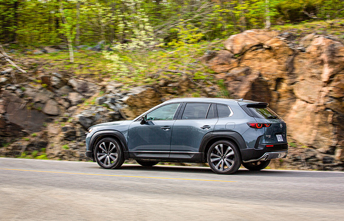 A Mazda CX-50 driving down a road lined with trees