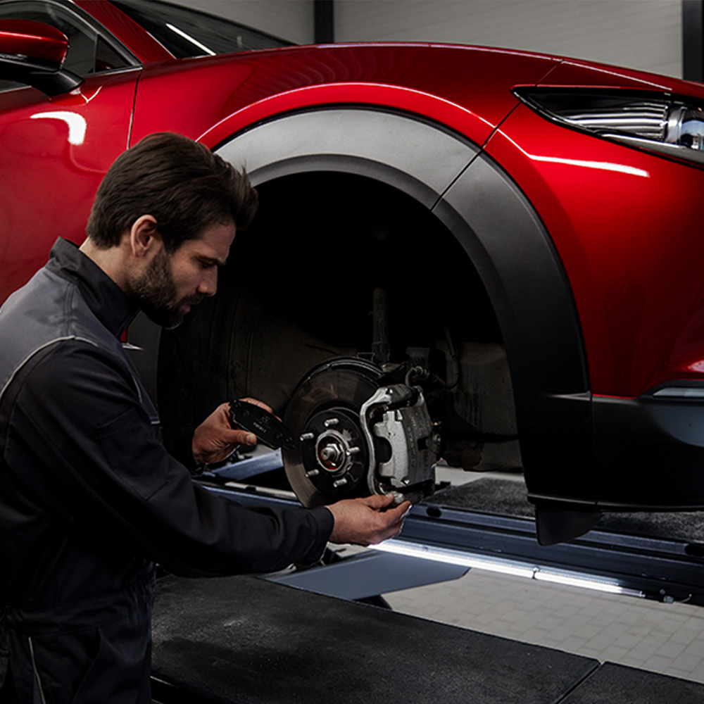 A Mazda technician working on a vehicle's brakes