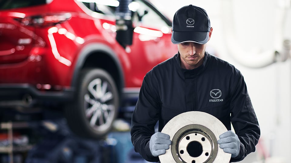 A Mazda technician working on a vehicle's brakes