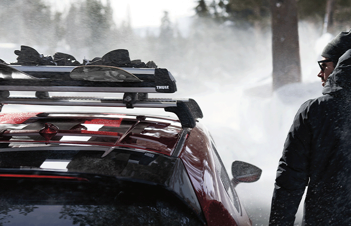 Un homme debout à côté d’une Mazda3 avec un porte-planche à neige monté sur le toit