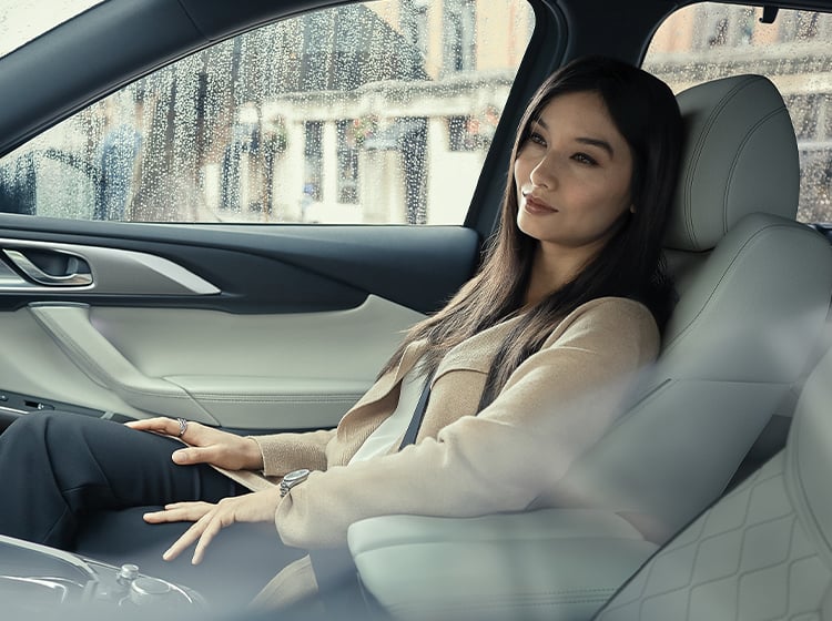 Femme bien habillée installée confortablement dans le siège passager d’un Mazda CX-9, d’où l’on voit des gouttes de pluie dans la glace.