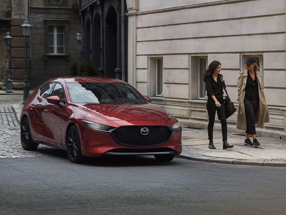 Femme longeant un VUS Mazda rouge stationné, près du mur de briques d’un édifice victorien