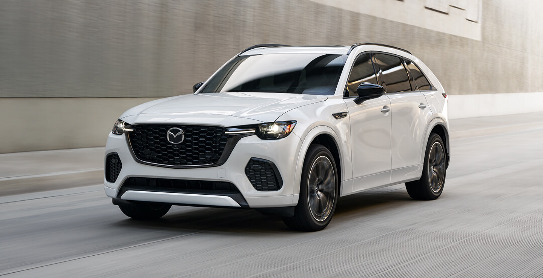 ¾ front image of Rhodium White Metallic Mazda CX-70 MHEV driving in sunken concrete highway.