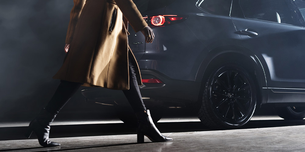 Elegantly dressed woman strides past Polymetal Grey Metallic CX-9 at night