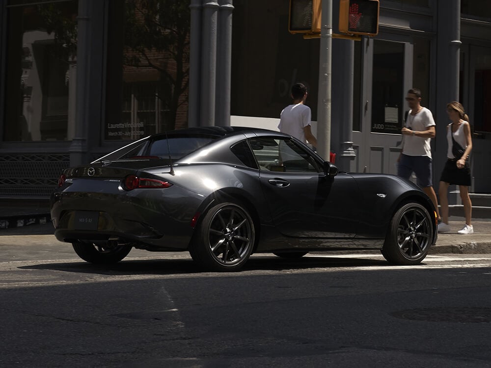 Mazda MX-5 RF drives past pedestrians on a sunny summer’s day.