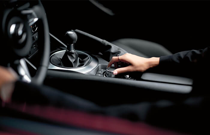 La main d’une femme qui ajuste le bouton du poste de contrôle HMI dans l’habitacle de la Mazda MX-5 à toit souple.