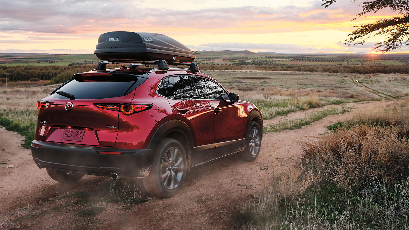 Soul Red Crystal Metallic Mazda CX-30 drives away on an open dirt road.