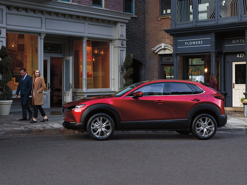Une femme se retourne sur le Mazda CX-30 rouge vibrant cristal métallisé garé devant une boutique.