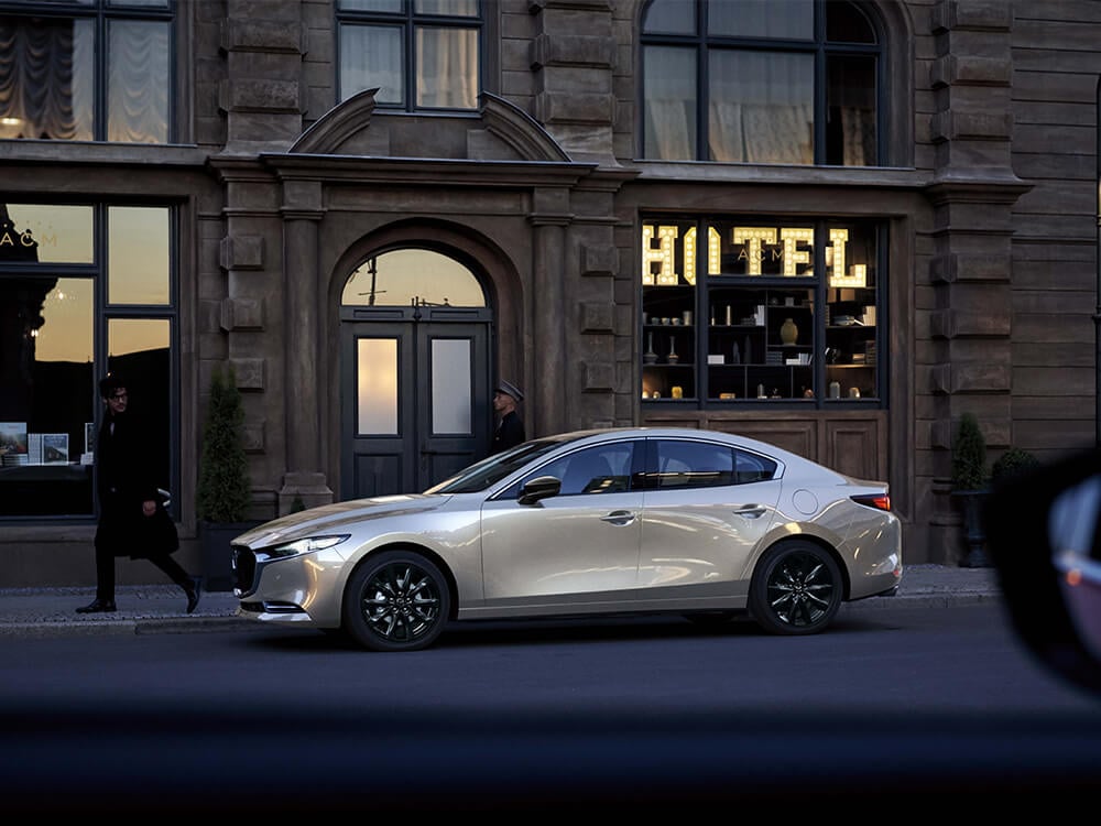 Platinum Quartz Metallic Mazda3 parked outside hotel at dawn.