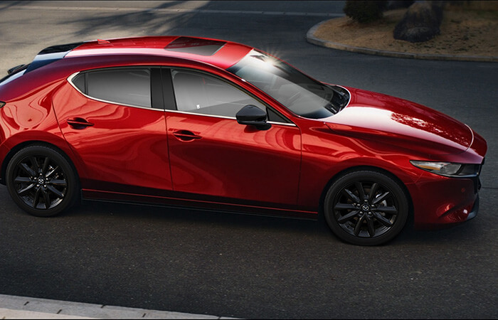 Une Mazda3 Sport rouge vibrant cristal métallisé, en mouvement dans une rue de la ville.