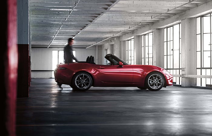 Driver approaches Mazda MX-5 Soft Top with top down in daylit parking garage.