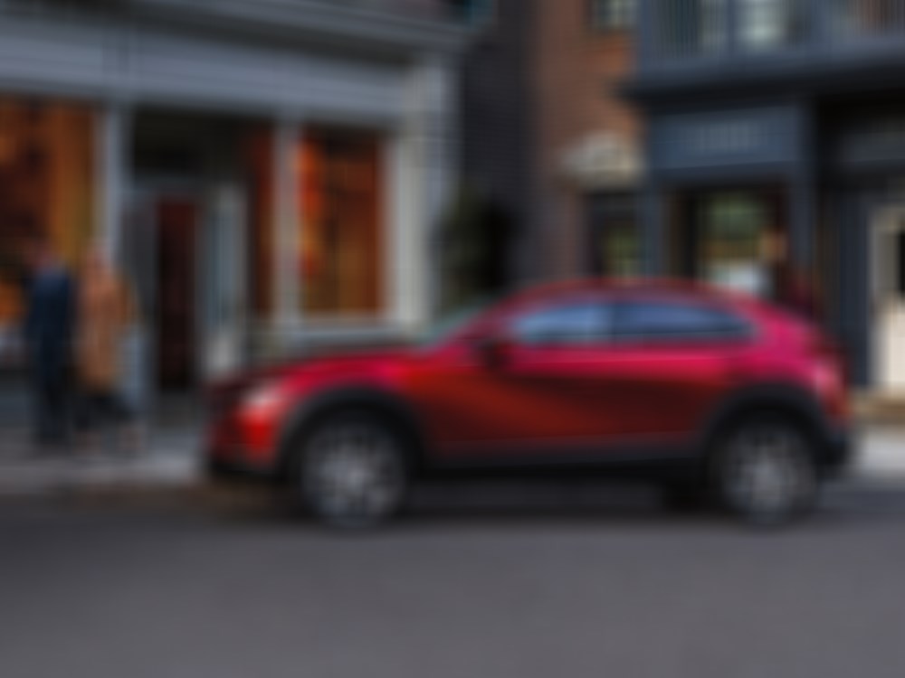 Woman looks back at Soul Red Crystal Metallic Mazda CX-30 parked out front of boutique. 