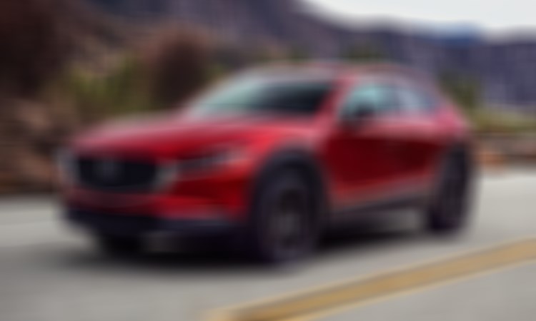 Un Mazda CX-30 rouge vibrant cristal métallisé parcourt une route montagneuse. 