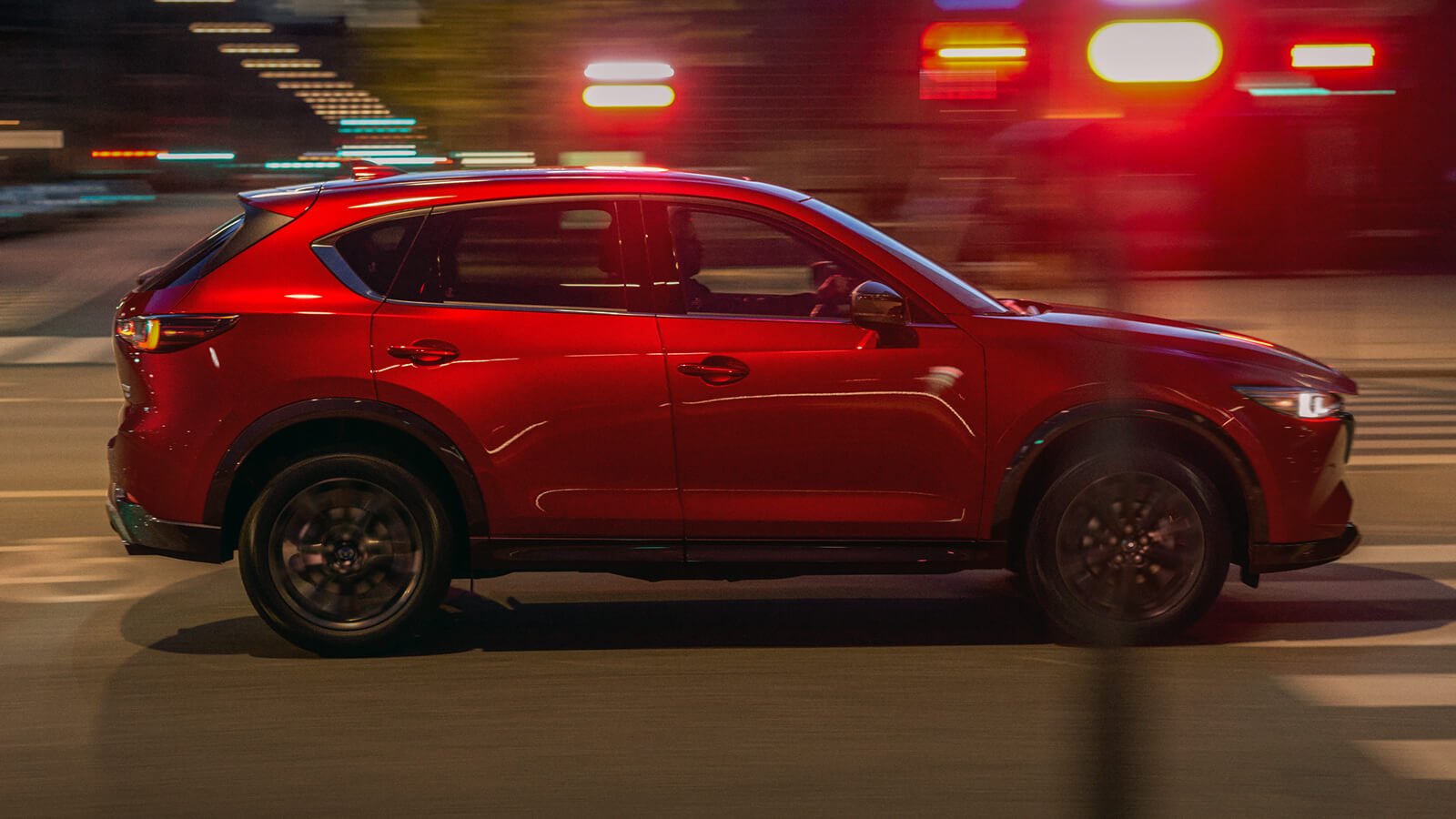 Soul Red Metallic CX-5 driving through a city at night. 