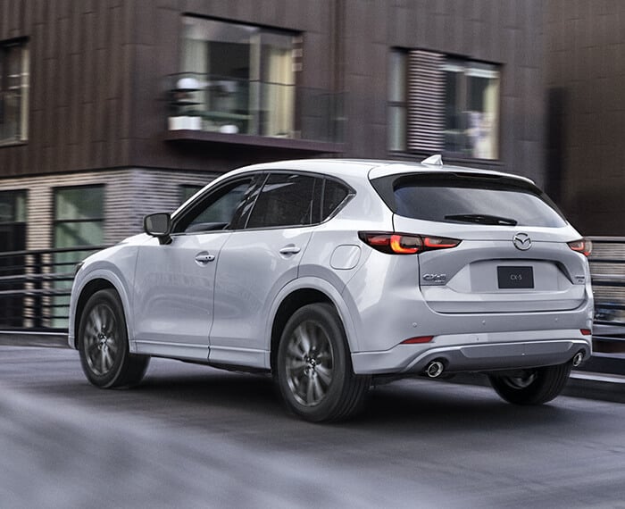 Rhodium White Metallic Mazda CX-5 driving on overpass with apartment building overlooking the road. 