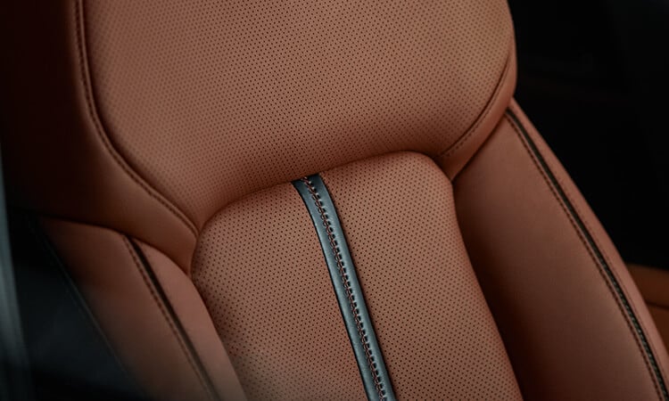 Close-up of terracotta leather backrest with orange stitching. 