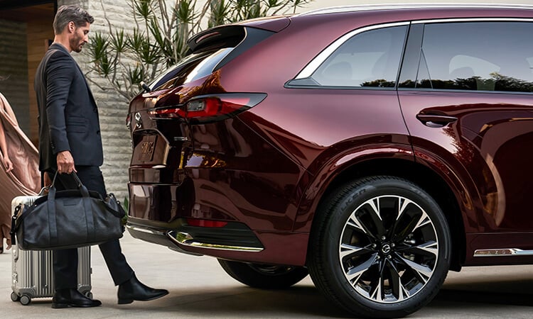 A man with hands full uses foot to activate hands-free power liftgate on Artisan Red CX-90.