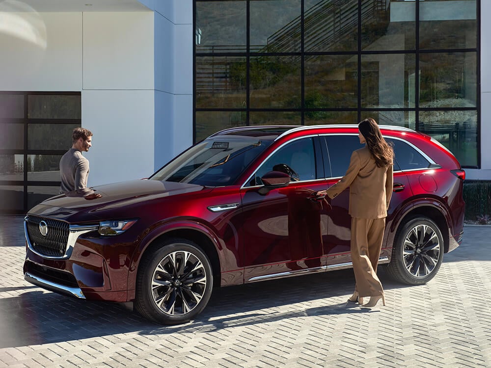 Driver in tan suit reaches for driver’s seat door of Artisan Red CX-90 PHEV.