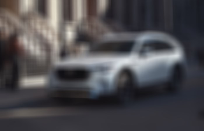 Un Mazda CX-90 garé dans une rue de la ville; la lumière du matin éclaire les appartements en arrière-plan.   