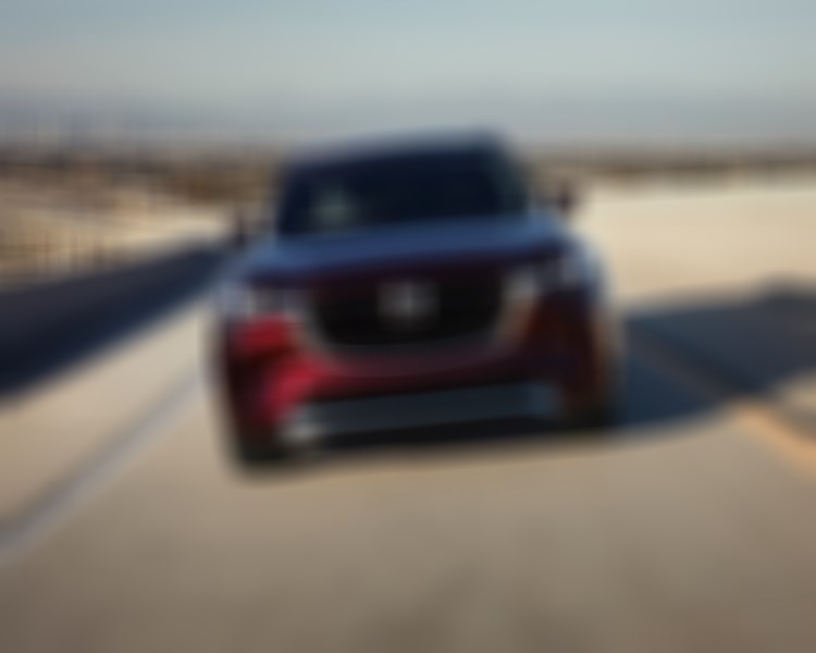Artisan Red CX-90 casts a shadow on concrete highway overpass as it approaches. 