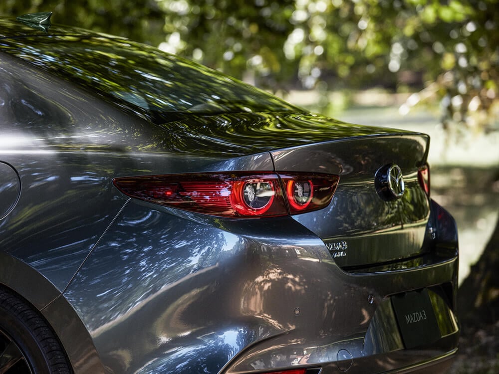 Mazda3 Sedan parked in verdant park, close up of taillights on sunny summer day. 