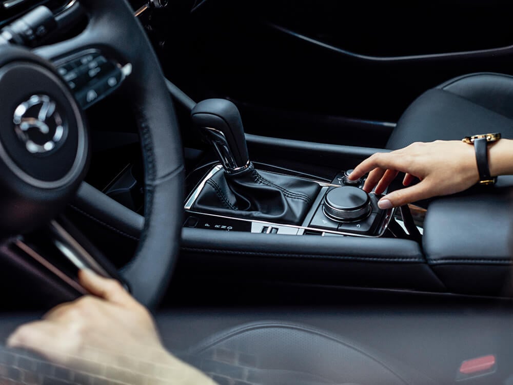 Mazda3 sedan cockpit, driver’s hand reaches for HMI Commander Control in the centre console.