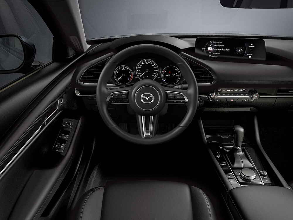 Vue de la cabine de la Mazda3 Sport montrant le volant, la console centrale HMI et les écrans du tableau de bord.