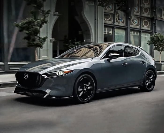 Mazda3 Sport drives down city street, passing a hotel’s large arched entryway. 