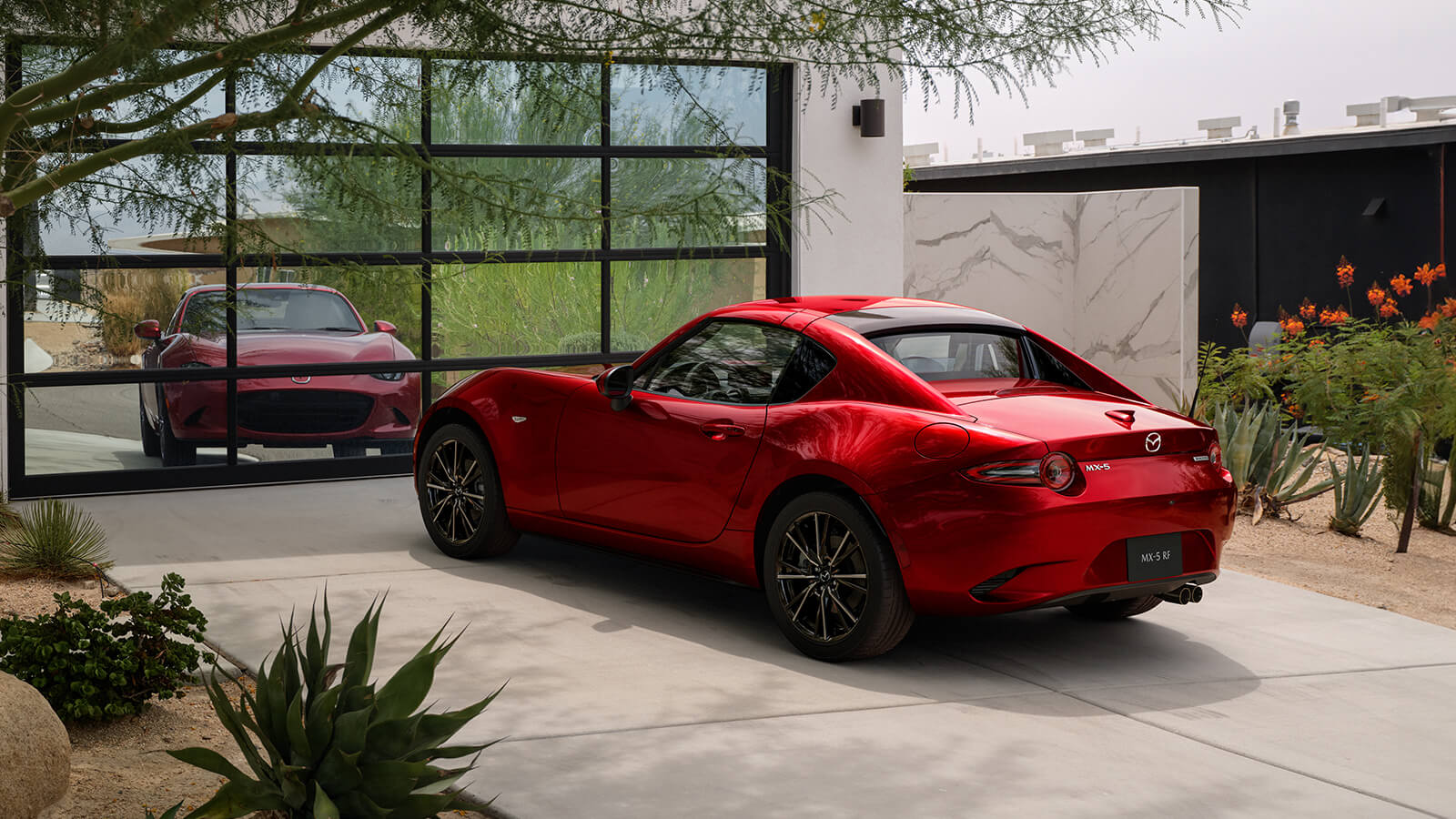 Soul Red Crystal Metallic MX-5 RF parked in front of a reflecting garage, showcasing its sleek design on a driveway.